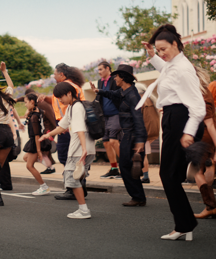A large group of happy people dancing in the street. A bus with the words "Feel Good" in the background.