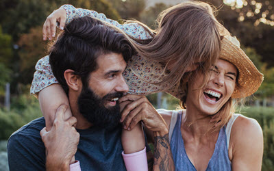 A young couple together with their daughter who is sat on her dad's shoulders