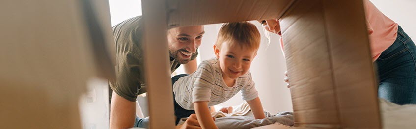 A mother and father and their child playing pretend with a cardboard box